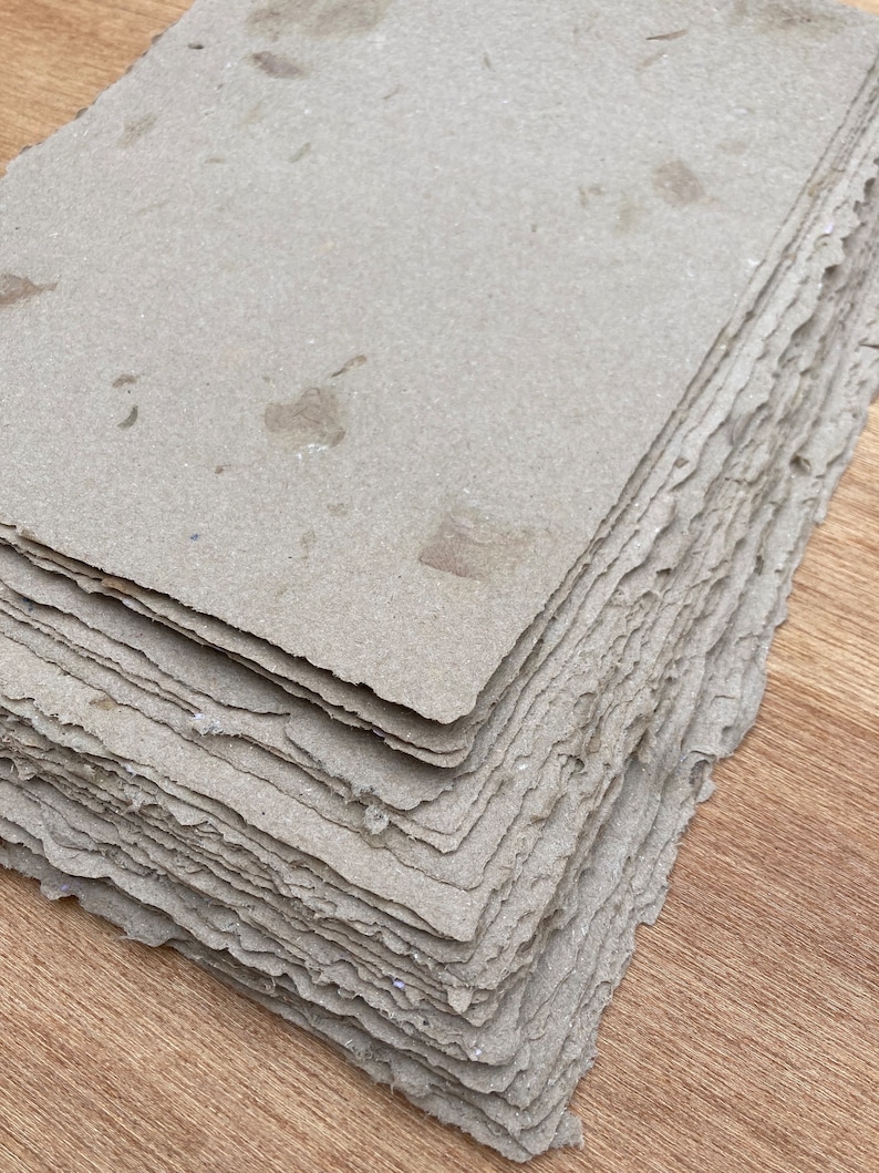 Puede incluir: Una pila de hojas de papel hechas a mano con una superficie rugosa y texturizada de color marr&oacute;n claro. El papel tiene un borde ligeramente irregular y parece estar hecho de materiales reciclados.