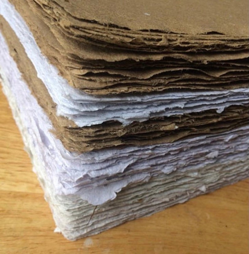Pu&ograve; includere: Un mucchio di fogli di carta fatti a mano in varie tonalit&agrave; di marrone e bianco. La carta ha una superficie ruvida e testurizzata ed &egrave; realizzata con materiali riciclati.
