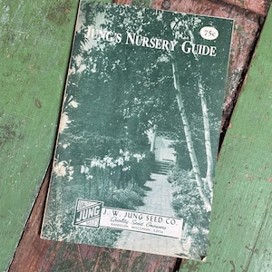 May include: A vintage Jung's Nursery Guide booklet with a dark green cover featuring a black and white photograph of a garden path. The text reads Jung's Nursery Guide, 75c, and J.W. Jung Seed Co. Quality Seed Growers, Randolph, Wisconsin 53956.