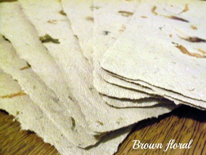 May include: A stack of handmade paper sheets with brown floral inclusions. The paper has a rough, textured surface.