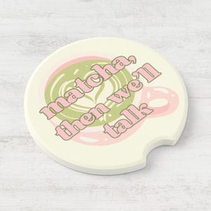 May include: Cream-colored car coaster with a matcha latte design. The coaster features a green matcha latte art design with pink accents and the text "matcha, then we'll talk" in pink lettering. The coaster has a curved cutout for easy removal.