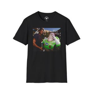 May include: Black t-shirt with a photo of a man in a black shirt standing next to a character from the Toy Story movie, Buzz Lightyear. The text "Buzz Lightyear" is written above the photo.