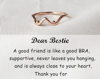 Puede incluir: Un anillo de oro rosa con un diseño ondulado y dos pequeñas esferas. El anillo está sobre un fondo a rayas blanco y gris. El texto "Dear Bestie" está encima de una cita sobre la amistad.