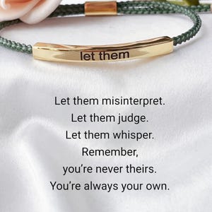 Può includere: Un braccialetto color oro con le parole "let them" incise su una barra curva. Il braccialetto ha un cordoncino intrecciato verde. L'immagine include anche il testo: "Let them misinterpret. Let them judge. Let them whisper. Remember, you're never theirs. You're always your own."