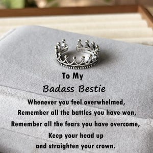 Op de afbeelding: Een zilveren kroonring met de woorden "To My Badass Bestie" en een boodschap over het herinneren van gewonnen gevechten en overwonnen angsten. De boodschap eindigt met "Keep your head up and straighten your crown."