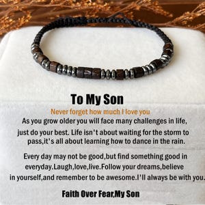 Op de afbeelding: Een zwart gevlochten armband met donkerbruine en zilverkleurige kralen. De tekst "To My Son" en een motiverende boodschap staan eronder.