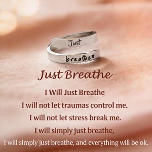 Puede incluir: Un anillo plateado con las palabras "Just breathe" grabadas. El anillo tiene un diseño envolvente. La imagen también incluye el texto "Just Breathe" y una cita motivacional sobre la respiración.