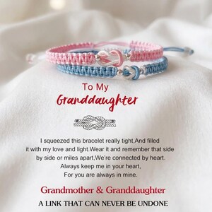 Może przedstawiać: Dwie bransoletki z makramy, jedna różowa i jedna niebieska, ze srebrnymi zawieszkami w kształcie węzłów. Tekst brzmi "To My Granddaughter" i wiadomość od babci do wnuczki. Bransoletki leżą na białej, teksturowanej powierzchni.