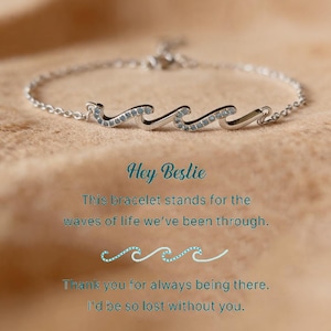 May include: A silver bracelet featuring a wave design with small, sparkling accents. The bracelet is on a neutral-toned surface, with the text "Hey Bestie" and a message about friendship.