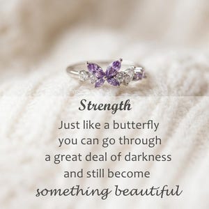 May include: A silver ring featuring a butterfly design with purple and clear gemstones. The image includes the word "Strength" and a quote about transformation.