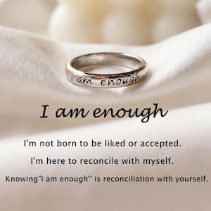 May include: A silver ring with the inscription "I am enough" is displayed on a white fabric. The image also includes the text "I am enough" and inspirational quotes about self-acceptance and reconciliation.