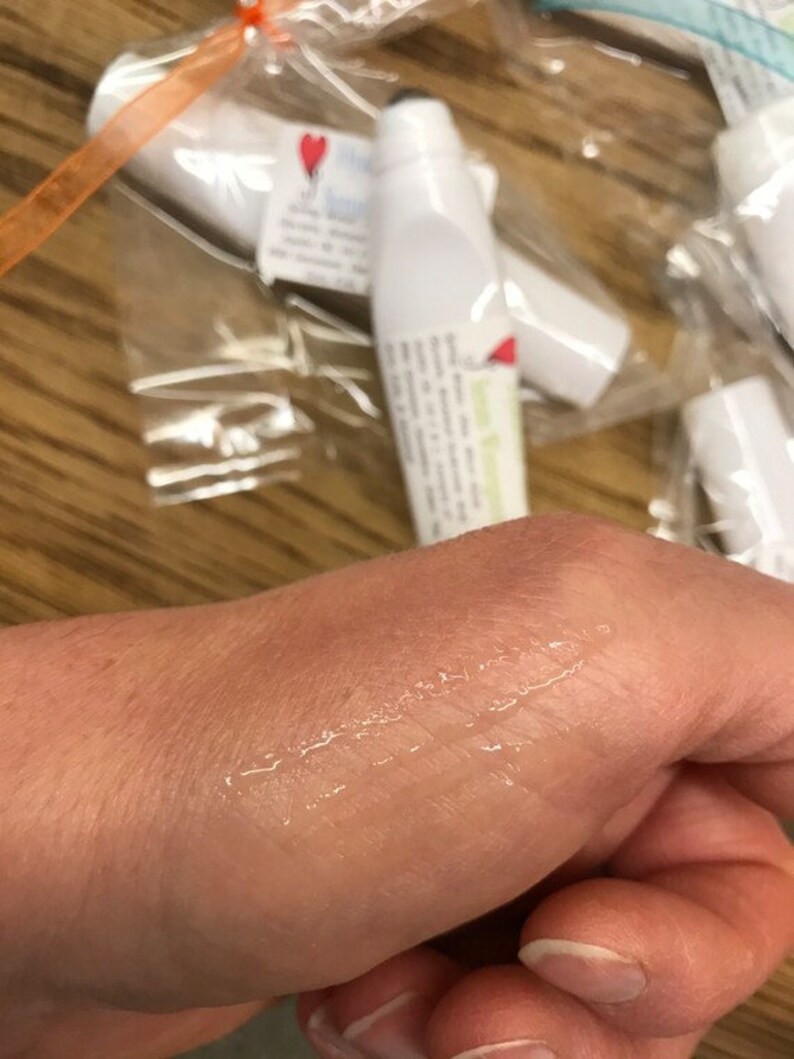 May include: A clear, viscous liquid is applied to a person's hand. The liquid is being applied from a white tube with a black cap. The tube has a label with the text "Lemon & Ginger" on it.