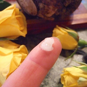 Puede incluir: Primer plano de una yema del dedo con una crema o loci&oacute;n blanca aplicada. El dedo est&aacute; delante de una rosa amarilla.