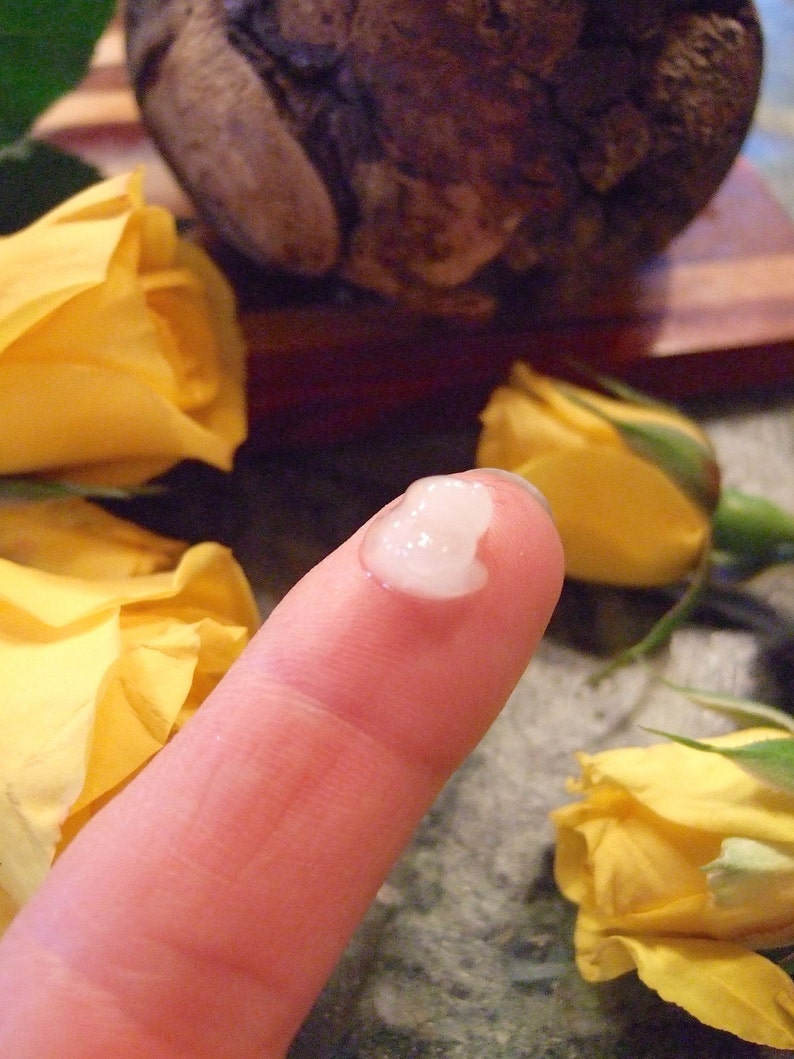 Puede incluir: Primer plano de una yema del dedo con una crema o loci&oacute;n blanca aplicada. El dedo est&aacute; delante de una rosa amarilla.