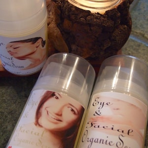 Puede incluir: Tres botellas de vidrio transparente con etiquetas que dicen "Eye & Facial Organic Serum" y "Facial Organic Serum". Las botellas est&aacute;n sobre una superficie de madera con una vela encendida en el fondo.