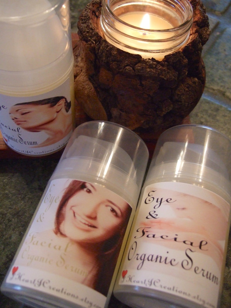 Puede incluir: Tres botellas de vidrio transparente con etiquetas que dicen "Eye & Facial Organic Serum" y "Facial Organic Serum". Las botellas est&aacute;n sobre una superficie de madera con una vela encendida en el fondo.