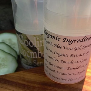 May include: Two clear plastic bottles with white labels. The label on the front bottle reads "Cooling Cucumber Facial Serum". The label on the back bottle reads "Organic Ingredients: Organic Aloe Vera Gel, Spring Water, Organic Extracts of Cucumber, Spirulina, Gotu Kola, Geranium, Dandelion, & Horsetail, Vitamin E, Jojoba Oil, Preservative Plantapon".