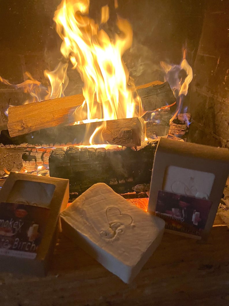 Puede incluir: Tres barras de jab&oacute;n artesanal delante de una chimenea. Las barras de jab&oacute;n est&aacute;n envueltas en papel marr&oacute;n con texto blanco. El texto en las barras de jab&oacute;n dice "Smokey Birch", "Lavender & Eucalyptus" y "Cranberry & Orange".