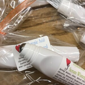 May include: Two white roller bottles with green and white labels. The labels contain text that reads "Hyaluronic Serum Winter" and "Hyaluronic Acid". The bottles are packaged in clear plastic bags with orange and blue ribbons.