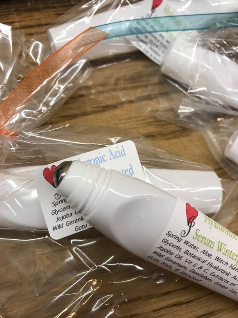 May include: Two white roller bottles with green and white labels. The labels contain text that reads "Hyaluronic Serum Winter" and "Hyaluronic Acid". The bottles are packaged in clear plastic bags with orange and blue ribbons.