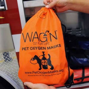 May include: An orange drawstring bag with the text "WAGN 02 FUR LIFE PET OXYGEN MASKS" and a black silhouette of a dog wearing an oxygen mask. The bag also includes the website address "www.PetOxygenMasks.org" and the tagline "Because the Pet's Life They Save May Be Your Own™".