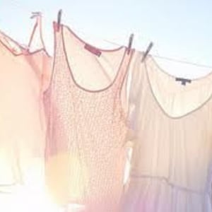 May include: Four white tank tops and a white dress hanging on a clothesline. The tank tops have different patterns and the dress has a simple design.