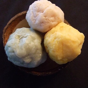 May include: Three round balls of soap in a coconut shell. The soap is white, light green, and yellow.
