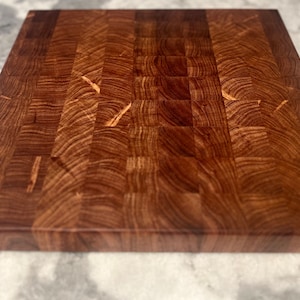 May include: A large, rectangular, wooden cutting board made of dark brown wood with a checkered pattern. The board has a smooth, polished surface and is perfect for chopping vegetables, fruits, and meats.