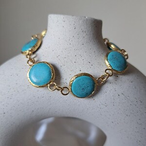 May include: A gold chain bracelet with turquoise round stones. The stones are set in gold and have a textured finish.