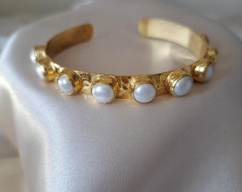 Puede incluir: Un brazalete de oro con acabado martillado y detalles de perlas blancas.