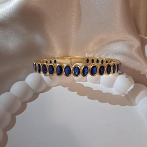 May include: A gold bangle bracelet with a row of oval-shaped blue gemstones.