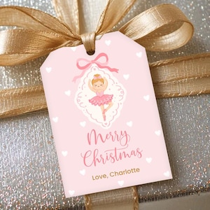 May include: A silver gift box with a gold ribbon and bow, topped with a pink gift tag. The tag features a ballerina illustration and the words "Merry Christmas, Love, Charlotte."