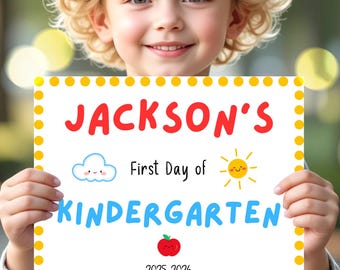 May include: A young child smiles while holding a sign that reads "Jackson's First Day of Kindergarten 2025-2026." The sign has a yellow border with yellow dots, and features a cloud, sun, and apple illustration.