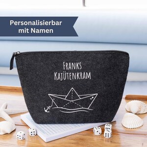 Könnte beinhalten: Graue Filztasche mit Reißverschluss und weißem Text "Franks Kajütenkram" sowie einem weißen Papierboot mit Anker und Herzmotiv.