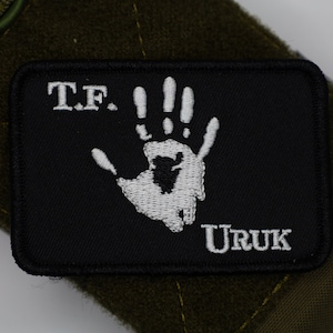 May include: Black patch with white embroidery of a handprint and the text "T.F. Uruk".