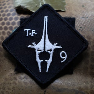 May include: Black diamond-shaped patch with white embroidered text "T.F. 9" and a white stylized image of a sword.