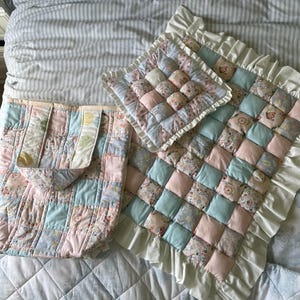 Könnte beinhalten: Ein Set aus drei gesteppten Artikeln in rosa und blauen Blumenmustern. Die Artikel umfassen eine Tragetasche, ein kleines Kissen und ein größeres Kissen mit einem Rüschenrand.
