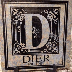May include: A slate tile with a black border and a decorative design featuring the letter "D" and the name "DIER" with the text "est. 1981".