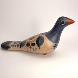May include: Hand-painted ceramic bird figurine. The bird has a blue head and tail, a tan body with black and brown leaf designs, and a red beak and feet. This decorative piece is a unique home decor item.
