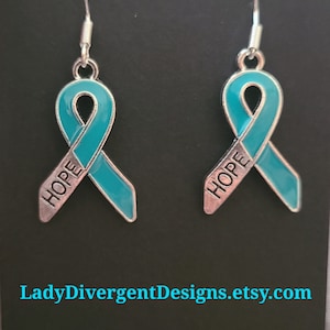 May include: Teal blue ribbon earrings with silver metal accents. The ribbon has the word "HOPE" written on it.