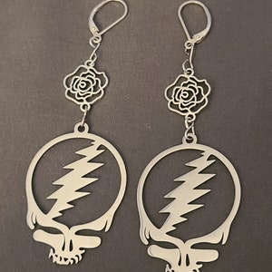 May include: A pair of silver earrings featuring a Grateful Dead Steal Your Face skull design with a lightning bolt and a rose charm.