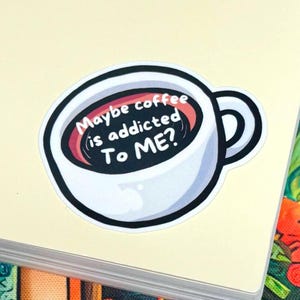 May include: A die-cut sticker featuring a white coffee mug filled with dark liquid. The text inside the mug reads, "Maybe coffee is addicted To ME?" in white, rounded lettering. The design has a thick black outline and a glossy finish.
