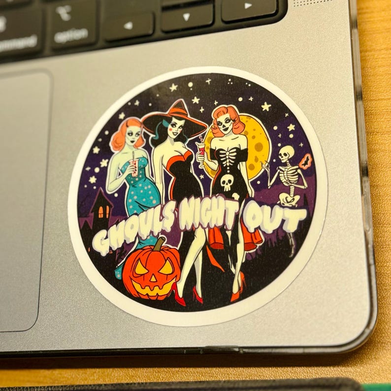 May include: A circular sticker featuring three figures in Halloween-themed attire, a skeleton, and a jack-o'-lantern against a starry night sky. The text GHOULS NIGHT OUT is printed in large white letters across the center of the illustration.