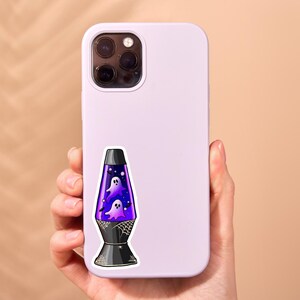 May include: A light purple smartphone case featuring a sticker of a lava lamp filled with purple liquid, two white ghosts, and small black bats. The base and top of the lamp are black with white spiderweb designs and a small spider illustration.