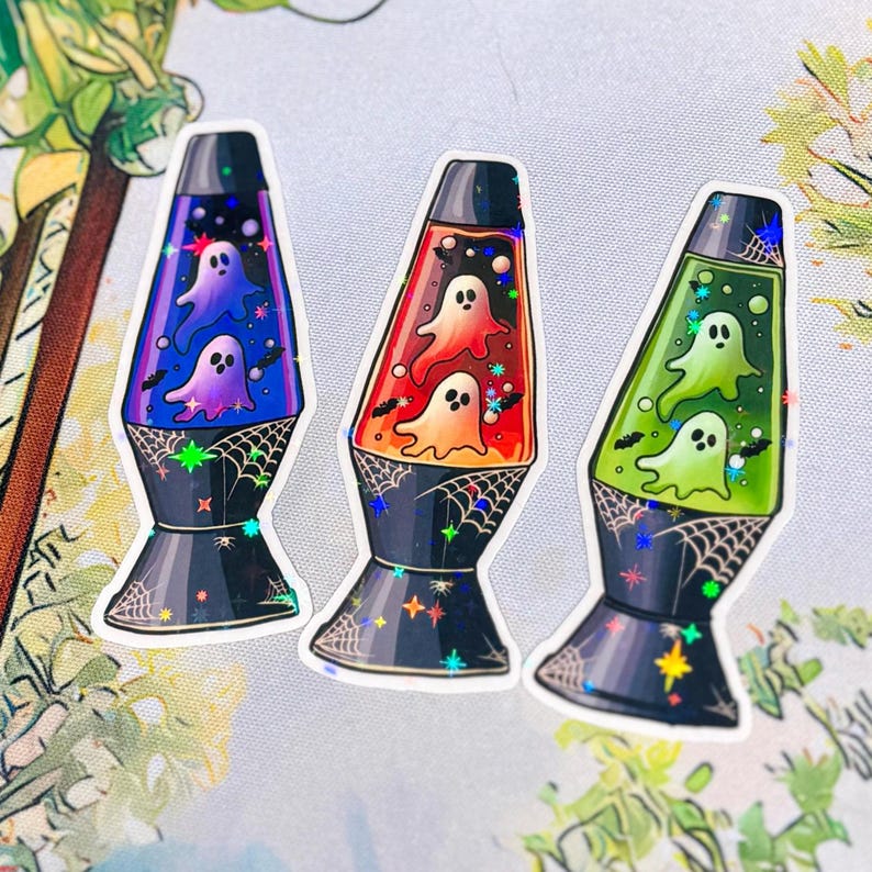 May include: Three holographic stickers shaped like lava lamps, each featuring two ghost figures inside. The lamps have black bases decorated with white spiderwebs and star-shaped sparkles. The liquid colors are blue, orange, and green.