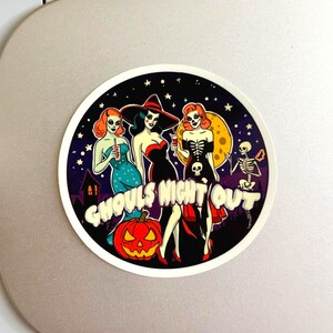 May include: A circular sticker featuring three stylized figures in Halloween attire, a skeleton, and a jack-o'-lantern against a starry night sky. The text GHOULS NIGHT OUT is printed in white, bold, bubbly letters across the center of the design.