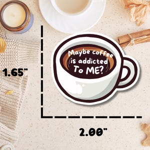 May include: A die-cut sticker shaped like a coffee cup with dark brown liquid inside. The text reads, "Maybe coffee is addicted To ME?". The sticker measures 1.65 inches in height and 2.00 inches in width as indicated by the visible measurement markings.