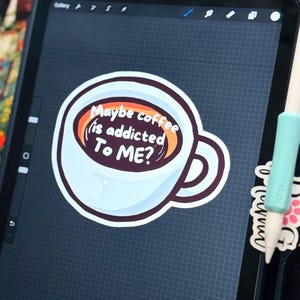 May include: A digital illustration of a white coffee mug filled with dark brown liquid, featuring the white text Maybe coffee is addicted To ME? inside the cup. The design is displayed on a tablet screen with a light blue stylus resting nearby.