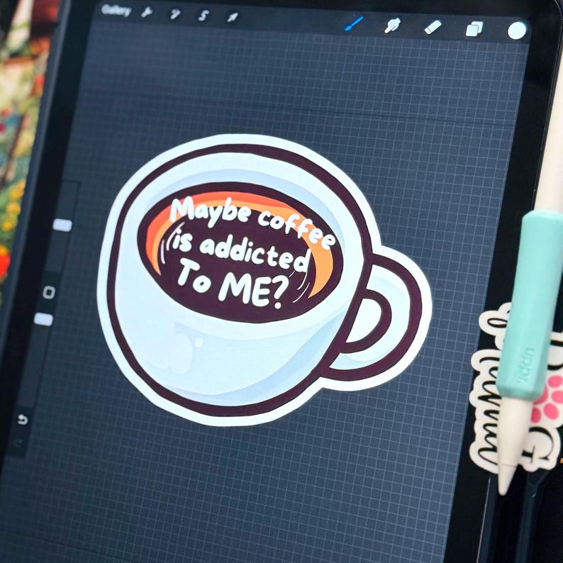 May include: A digital illustration of a white coffee mug filled with dark brown liquid, featuring the white text Maybe coffee is addicted To ME? inside the cup. The design is displayed on a tablet screen with a light blue stylus resting nearby.