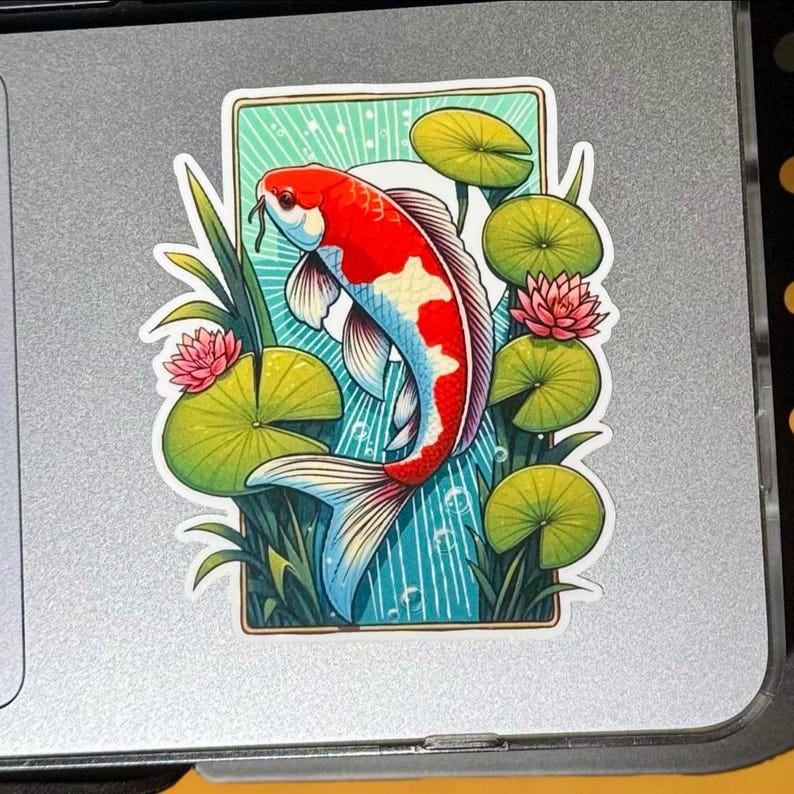 a rectangle shaped sticker of a koi fish swimming in a lilly pond, white sun and rays in background. the lillys stick out beyond the rectangle creating a 3D effect. the sticker is placed on a MAC laptop to the right of the trackpad.